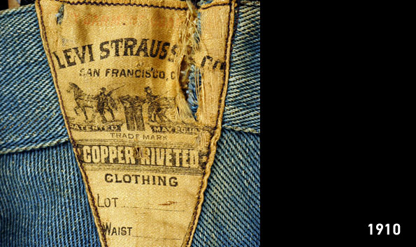 A distressed patch from 1910 on the back of a pair of denim jeans depicting the LS&Co. two-horse pull logo featuring the text "Levi Strauss * Co. San Francisco, CA" above an illustration of two horses attempting to pull apart a pair of pants.